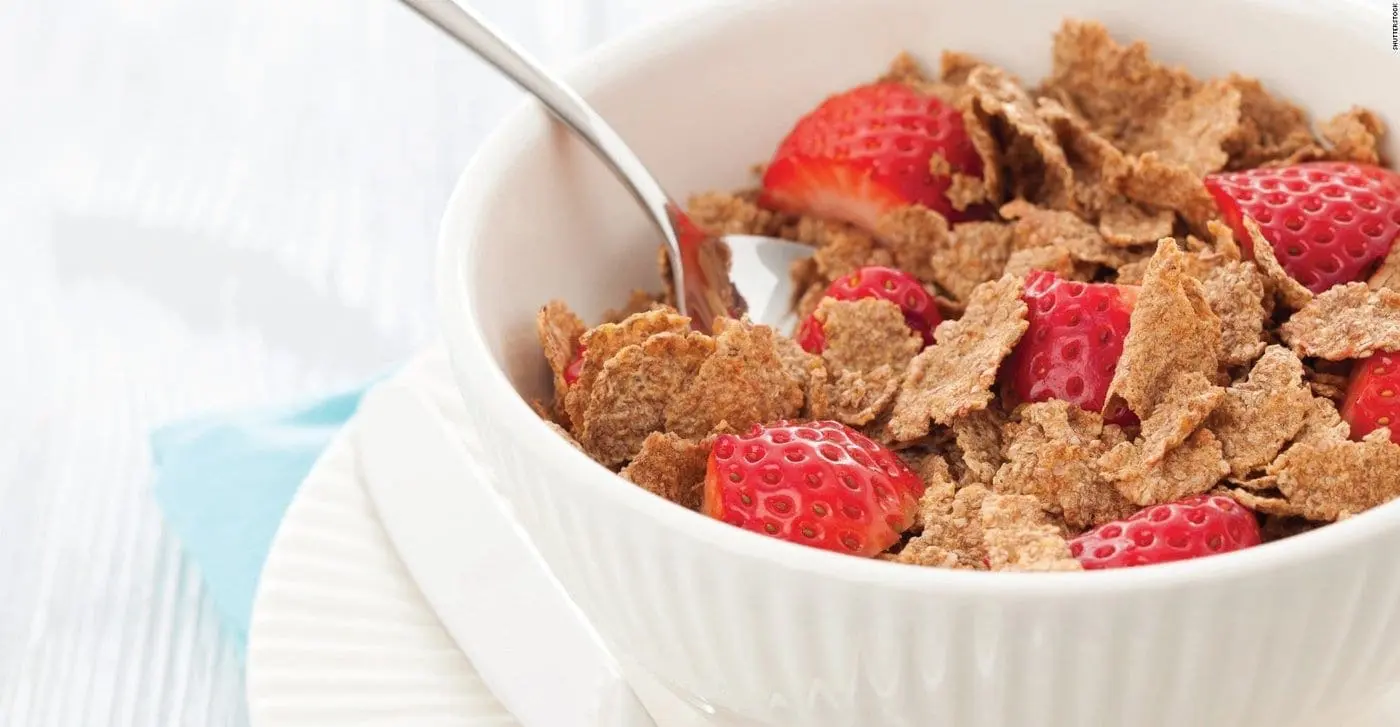 Bowl of whole grain cereal with sliced strawberries and a spoon.