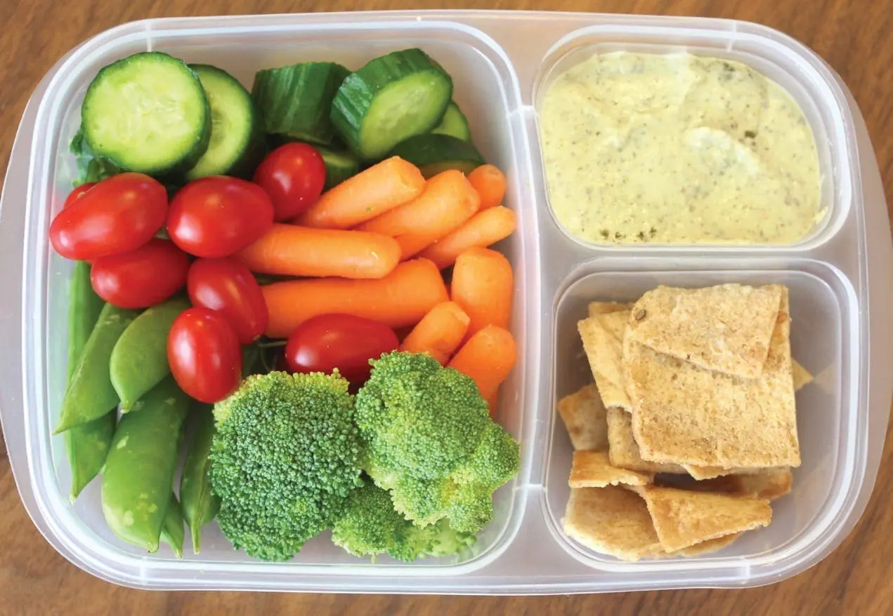 Bento box lunch with vegetables, hummus, and crackers.