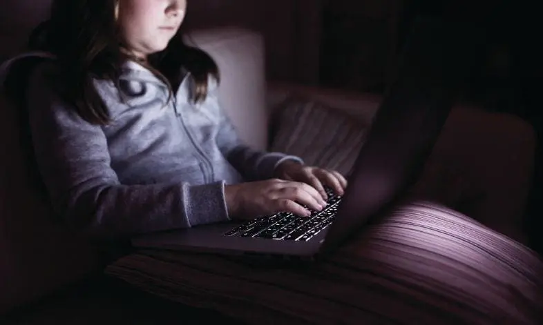 Child using a laptop in a dimly lit room.