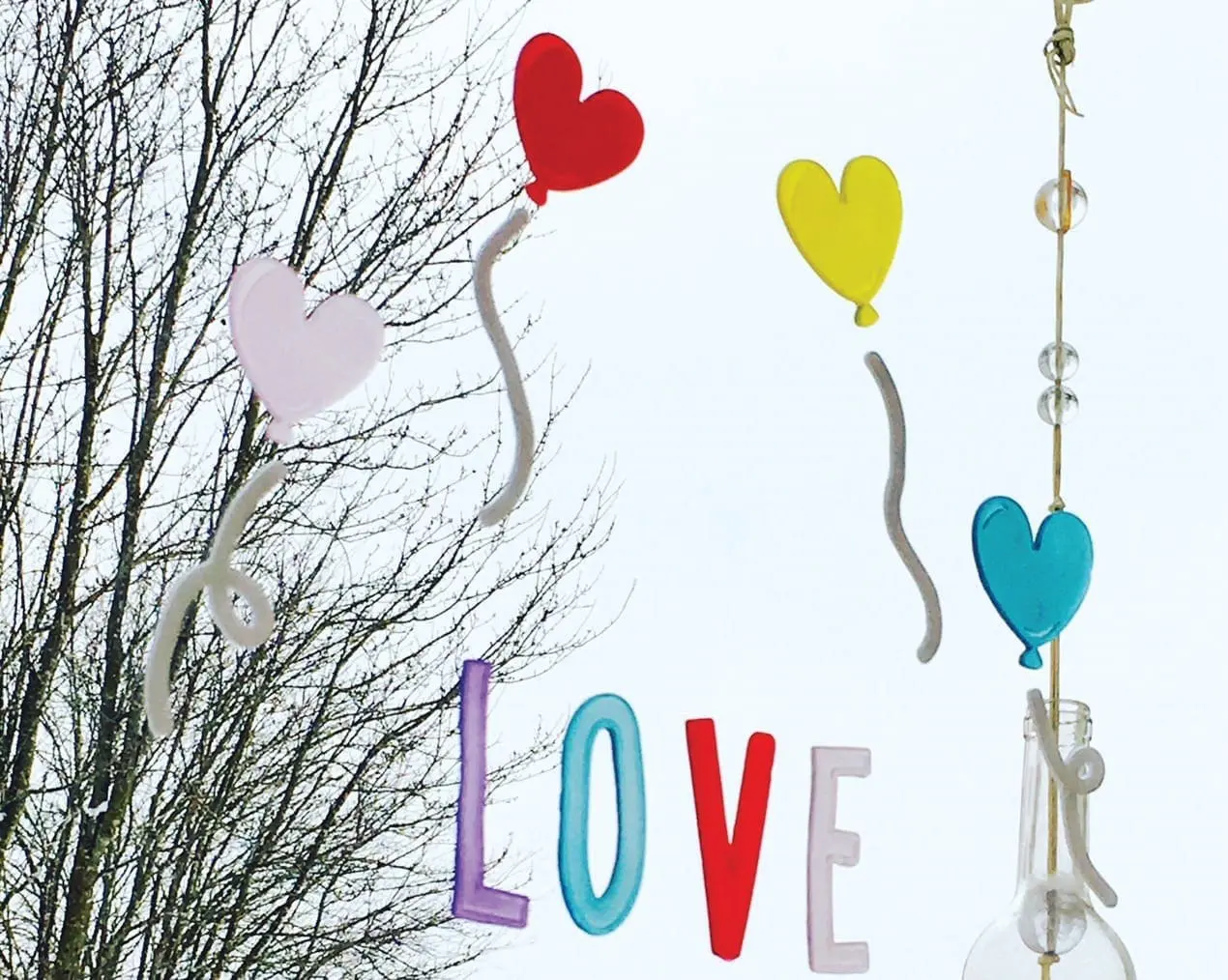 Three heart-shaped balloons and the word "LOVE" hanging in front of bare tree branches