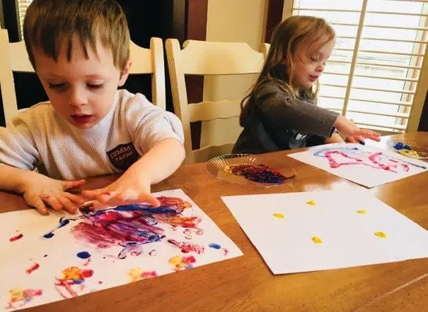 Two children painting at a table with papers and art supplies.