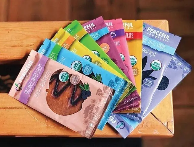 Colorful wrappers of Peaceful Fruits snacks fanned out on a wooden surface.