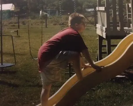 A boy climbs a yellow slide in a backyard.