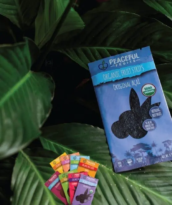 A package of Peaceful Fruits organic fruit strips surrounded by lush green leaves