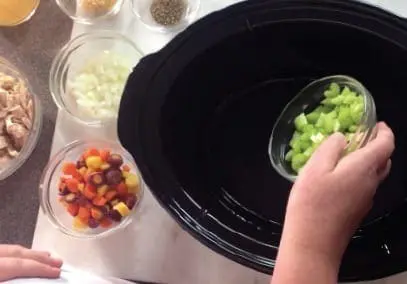 Diced celery being added to a slow cooker with other ingredients nearby.