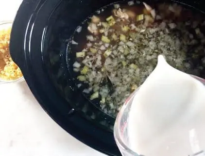 Slow cooker filled with chicken soup ingredients, with a scoop of mashed potatoes on the side
