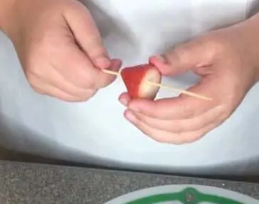 Hands threading a strawberry onto a wooden skewer.