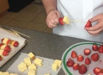 A person threads strawberries and pound cake onto a skewer.