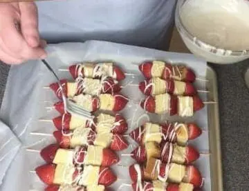 Strawberries and pound cake on skewers are drizzled with white icing.