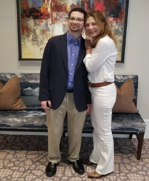 A man and woman stand in front of a patterned couch and abstract art.