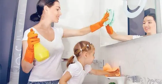 Mother and daughter cleaning a bathroom mirror and sink.