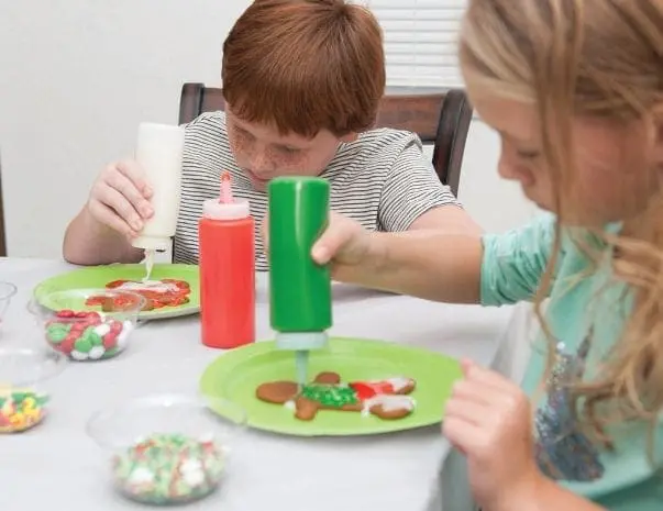 Children decorating cookies with frosting bottles and sprinkles.