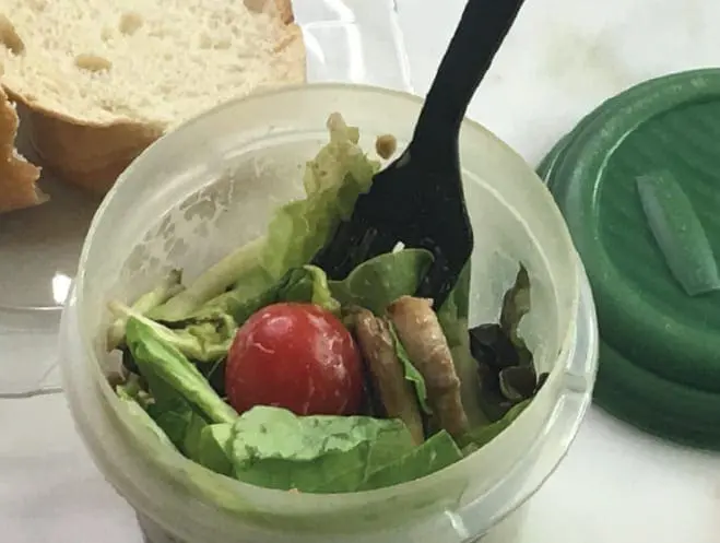 Plastic container filled with lettuce, a cherry tomato, and sunflower seeds with a fork inside.