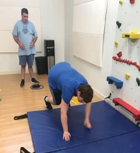 Two individuals are exercising in a room with a climbing wall.