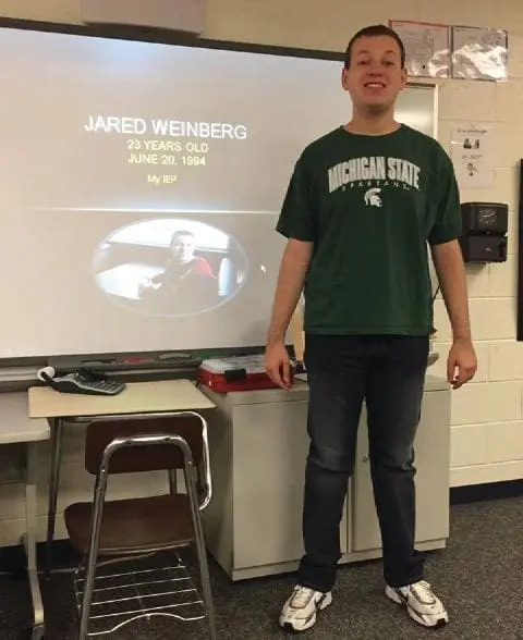 Jared Weinberg stands in front of a projector screen displaying his name and birth date.