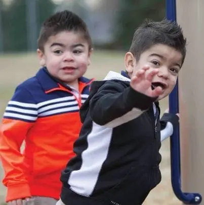 Two young boys on a playground, one reaching out his hand.