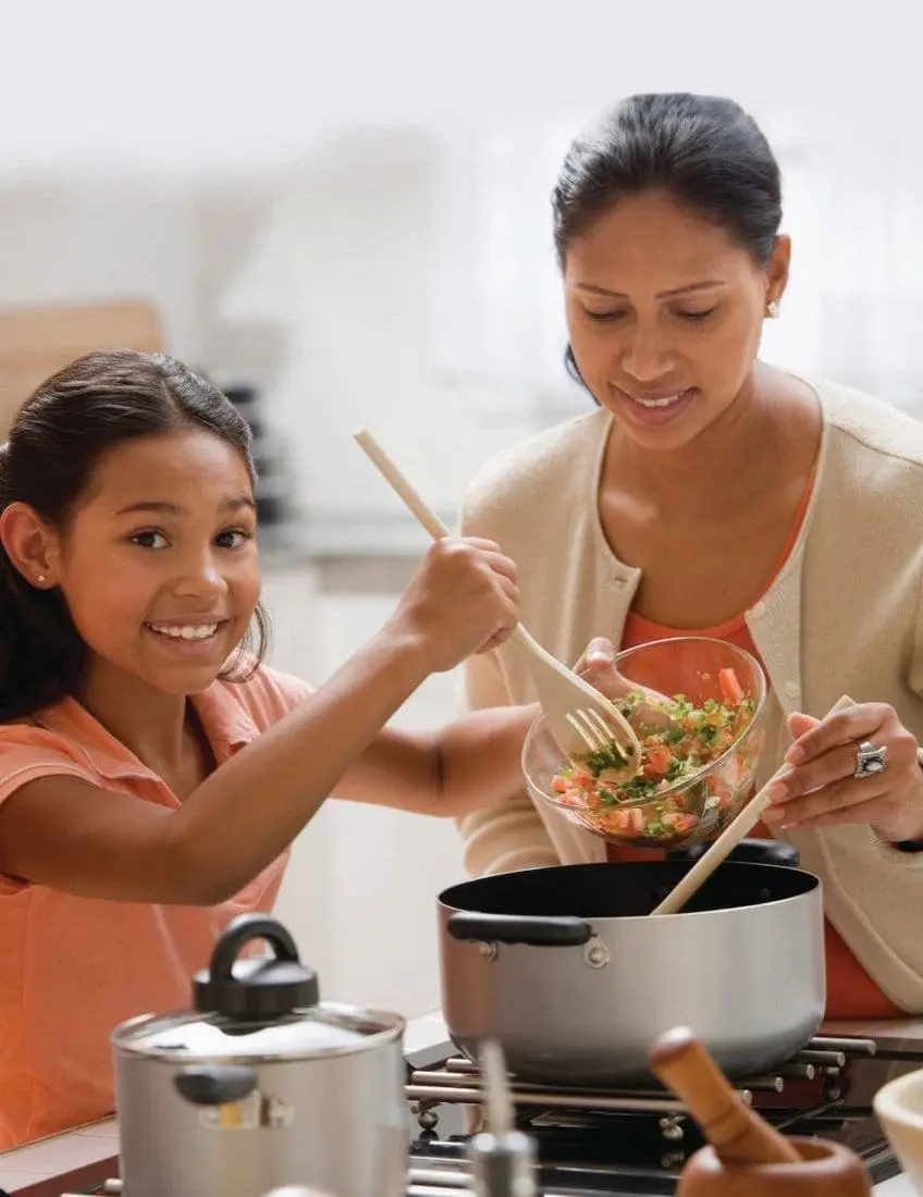 A mother and daughter prepare food together in a kitchen.