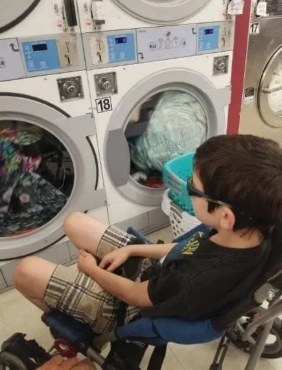 Child in a wheelchair watching laundry in a washing machine.