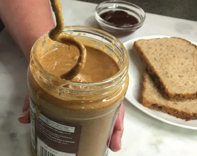 Peanut butter is stirred in a jar with a mixer attachment.