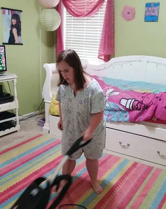 A young girl vacuums a colorful striped rug in a bedroom.