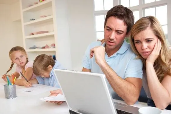 Parents looking stressed at a laptop while two children do schoolwork