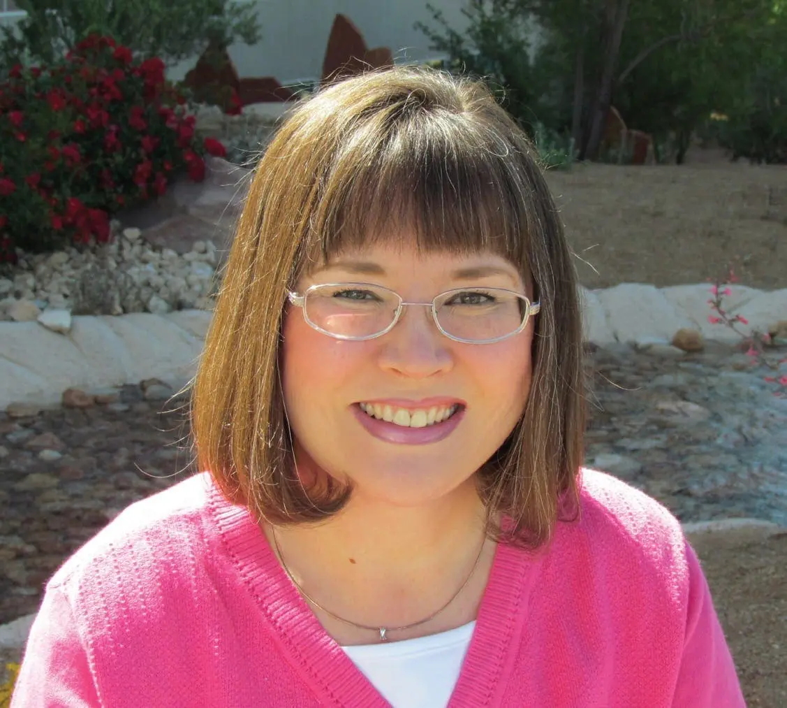 Diane smiling in a pink cardigan in a garden.