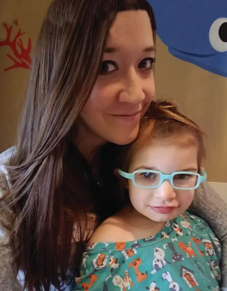 Kimberly smiles with her daughter Finley, who wears light blue glasses.