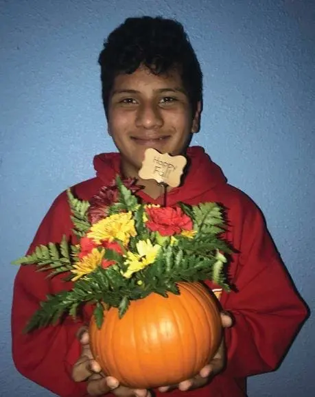 Young person in a red hoodie holding a small pumpkin with a floral arrangement.