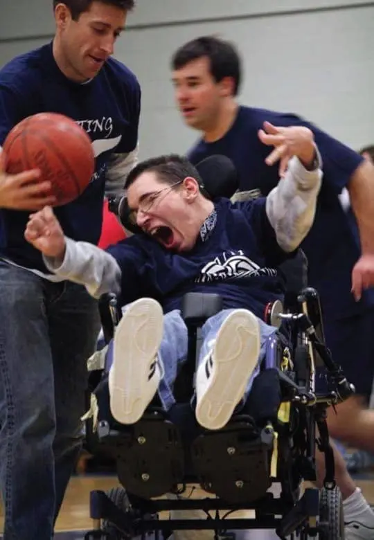A man in a wheelchair yells with excitement while playing basketball with two other men.