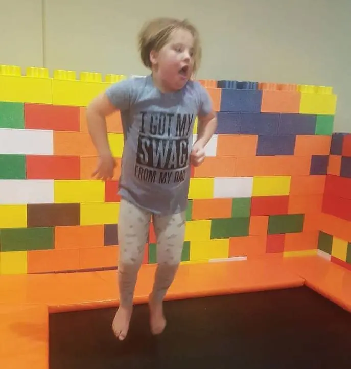 Young child in a t-shirt and leggings jumping on a trampoline.