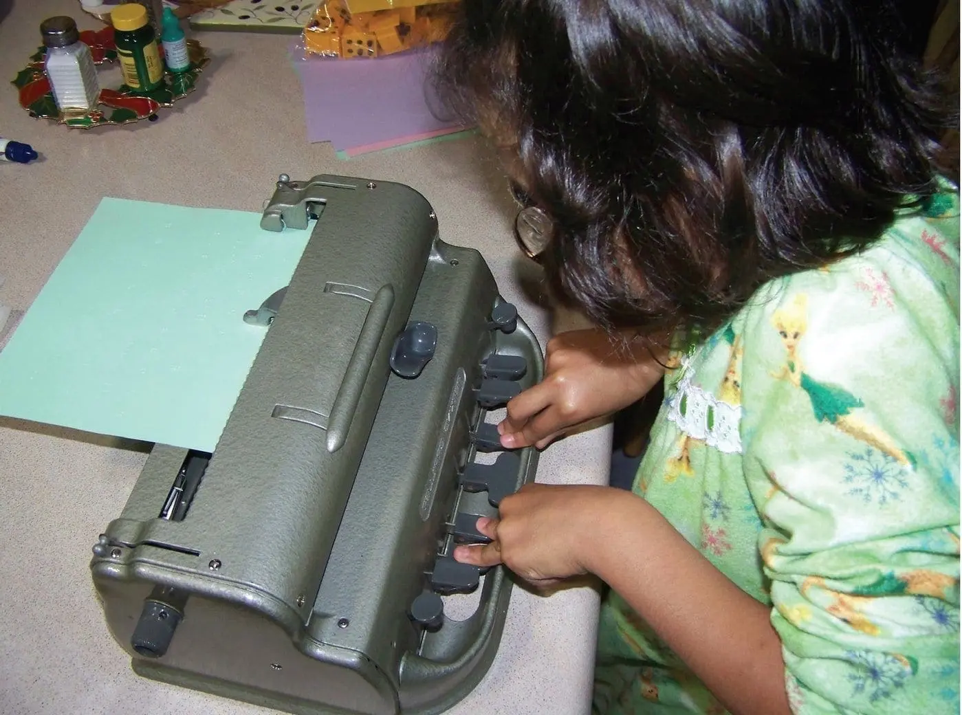 A person uses a braille embosser to print on green paper.