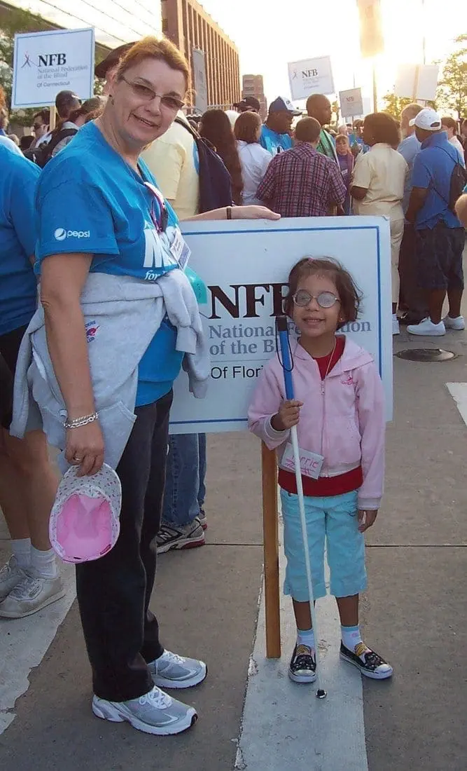 A woman and a young girl stand next to a sign that says "NFB National of the Blind of Florida.