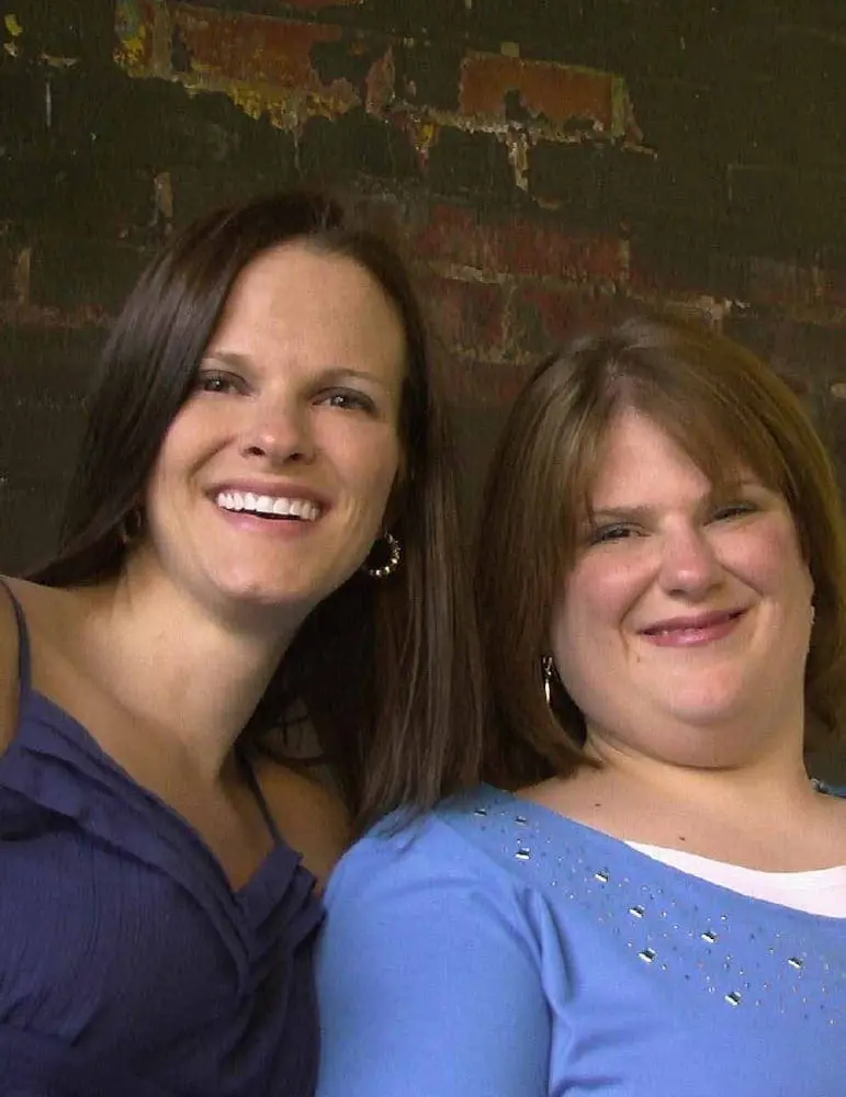 Angela Ruzicka and Amanda Angela smiling in front of a brick wall.