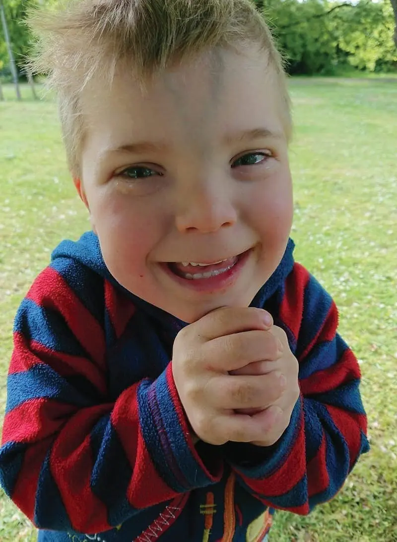Samuel smiling outdoors wearing a striped hoodie.