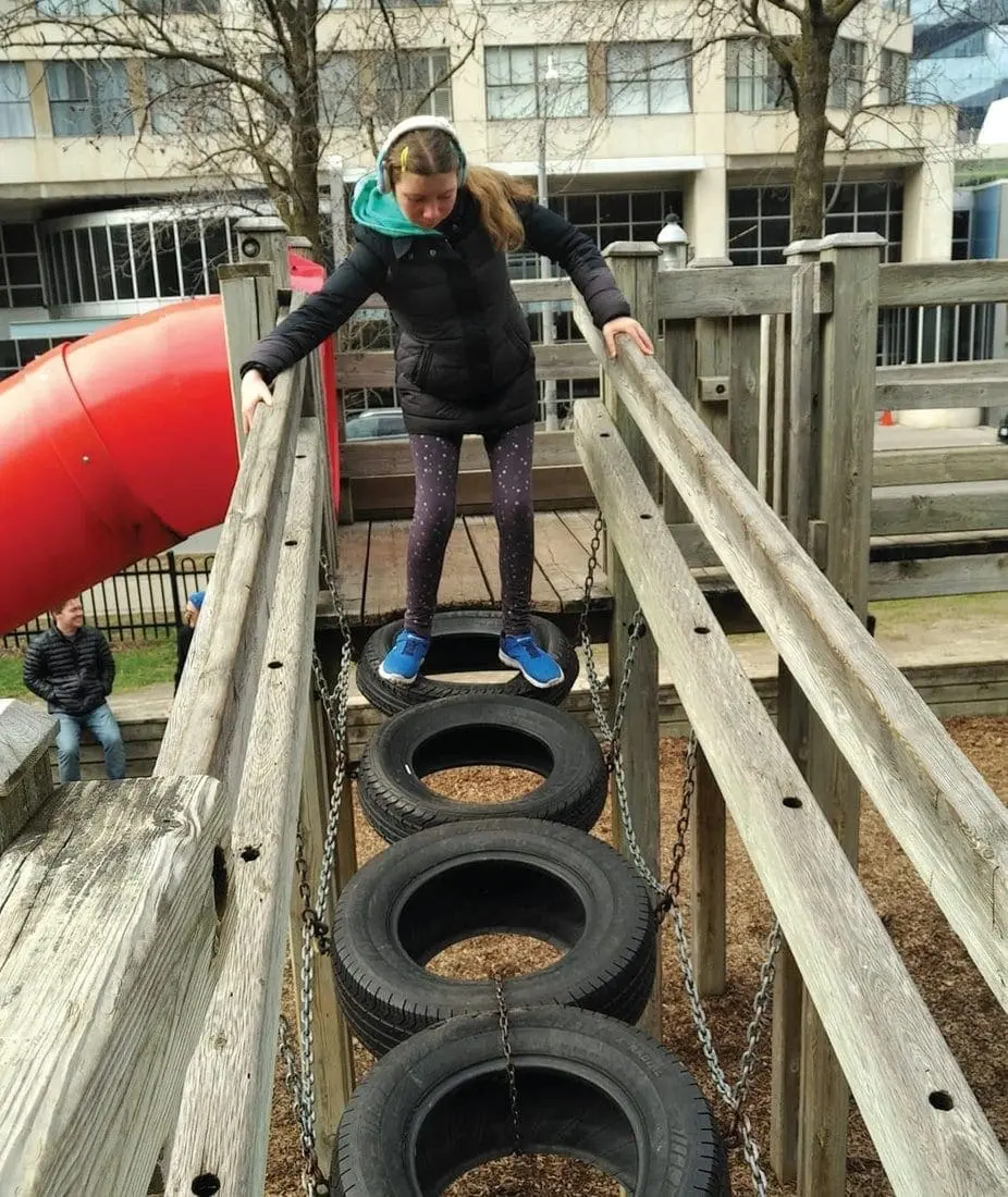 A young person walks across a rope bridge made of tires.