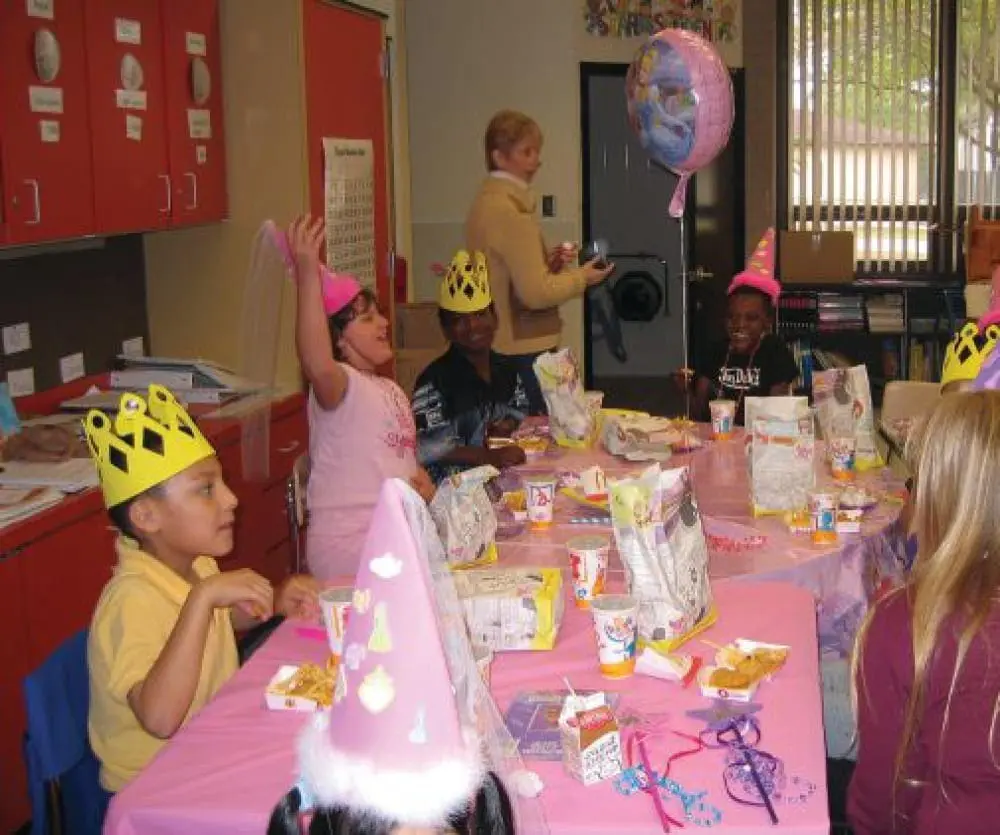 Children in party hats sit at a table in Mrs. Salisbury's second grade classroom.