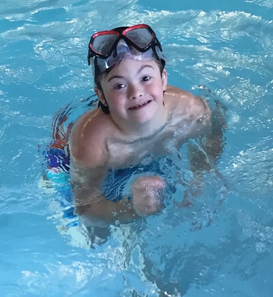 A child wearing goggles smiles while in a swimming pool.