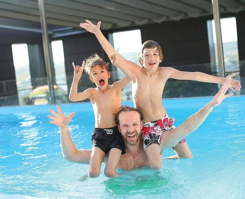 Three children and a man having fun in a swimming pool.