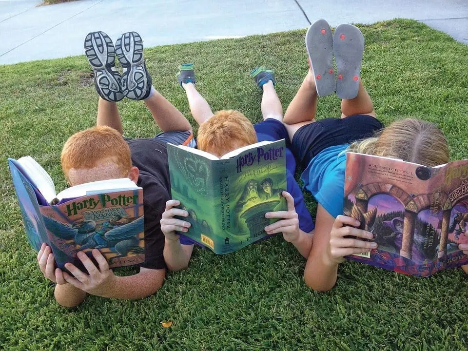 Three children lie on the grass reading Harry Potter books.