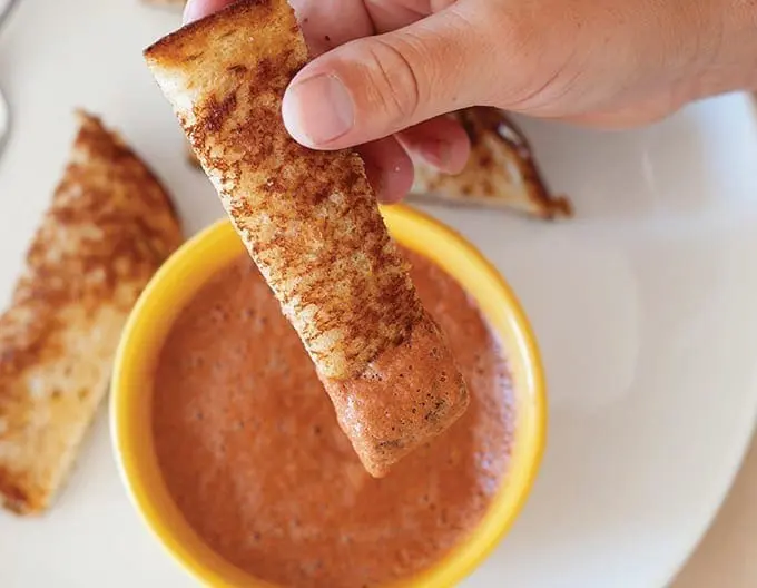 Grilled toast dippers being dunked into a bowl of tomato soup.