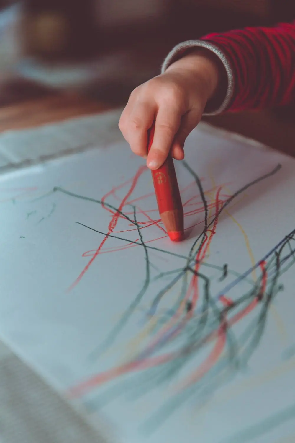 Child's hand holding a red crayon to draw on paper