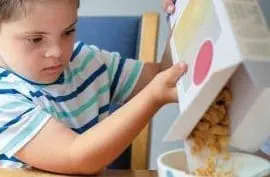 Child with Down syndrome pouring cereal into a bowl.