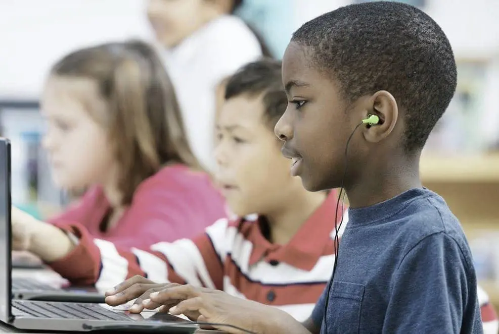 Children wearing earbuds and using laptops in a classroom.