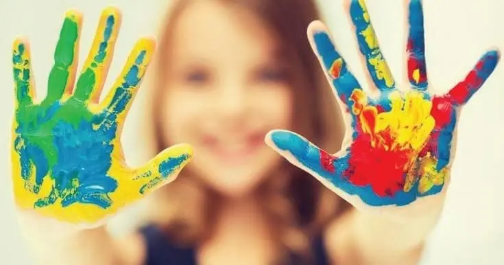 Child's hands covered in colorful paint, with the child blurred in the background.