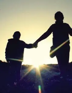 Silhouettes of two people holding hands against a sunset
