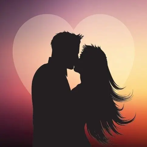 Couple kissing with a heart silhouette behind them at sunset