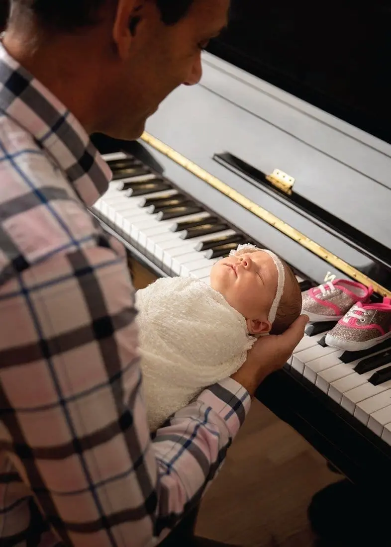 A man holds a baby next to a piano.