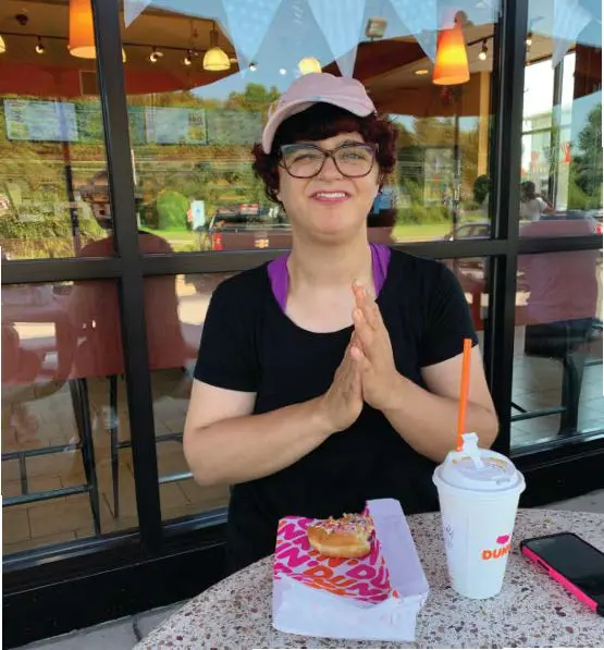 Elizabeth smiling with hands clasped at a table with a donut and drink