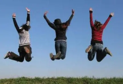 Three people jump with arms raised against a blue sky.