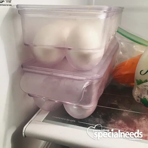 Clear plastic egg containers with white eggs inside, stacked in a refrigerator.